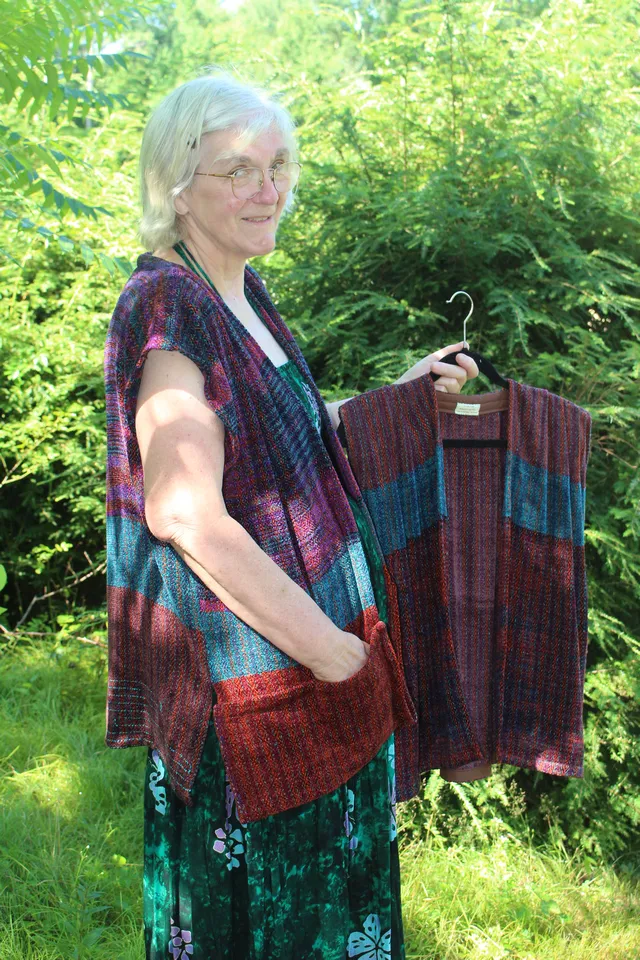 Woman wearing a striped red, pink, and turquoise vest and holding another striped vest