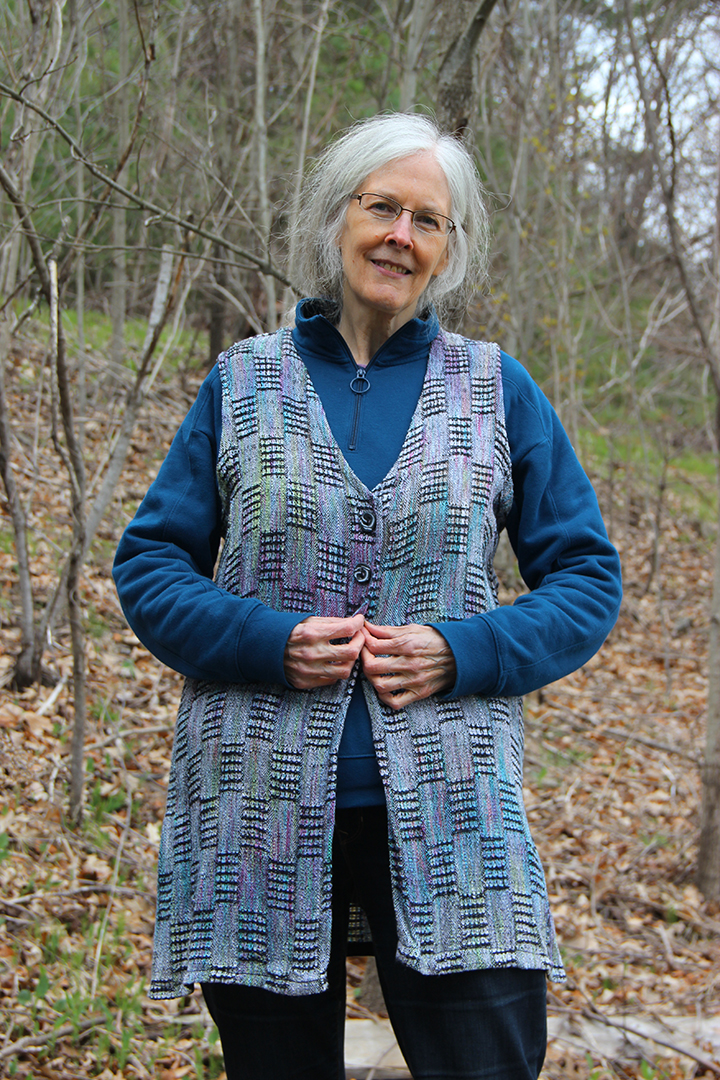 Woman wearing a long button-up vest in turquoise and pink over a sweatshirt