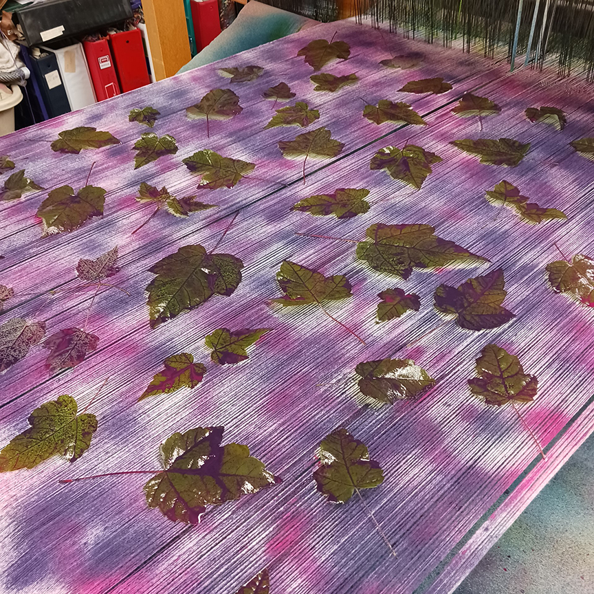 Leaves spread across the loom's warp, covered with pink and purple dye