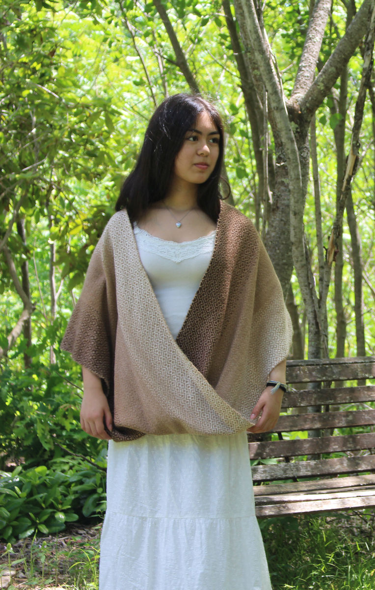 Young woman in a natural alpaca half-twist poncho in shades of brown over a long white dress