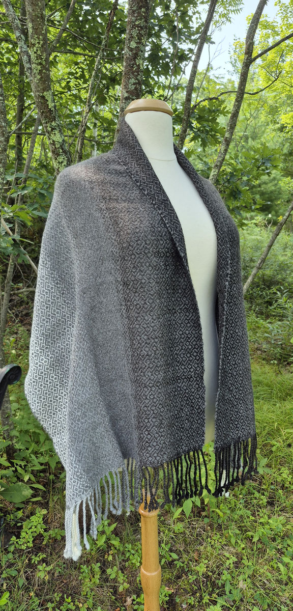 Natural alpaca shawl in shades of gray with fringe, on a dress form outdoors