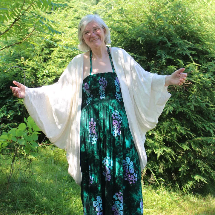 Woman in a large white cocoon over a long green dress, arms spread in a welcoming gesture