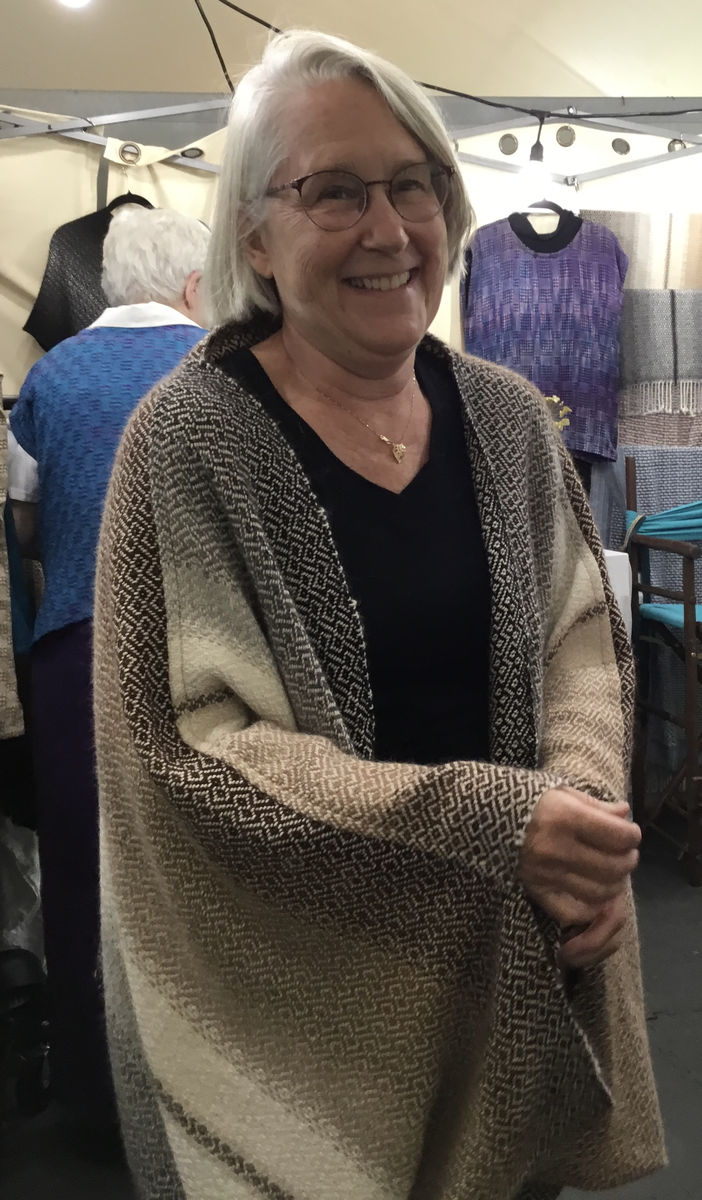 Woman at Frances's booth trying on a natural alpaca cocoon in brown, open at the front and covering her arms
