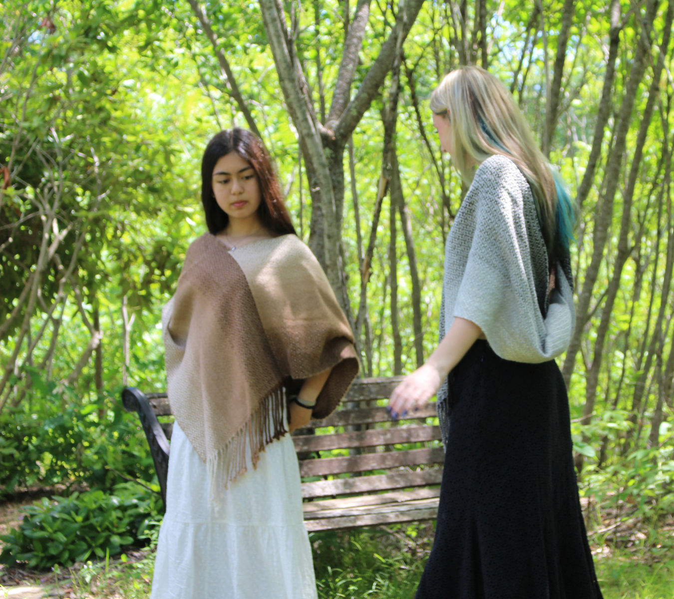 Young woman in a brown and cream natural alpaca full-twist poncho over a long white dress, beside a woman in a gray poncho over a long black dress